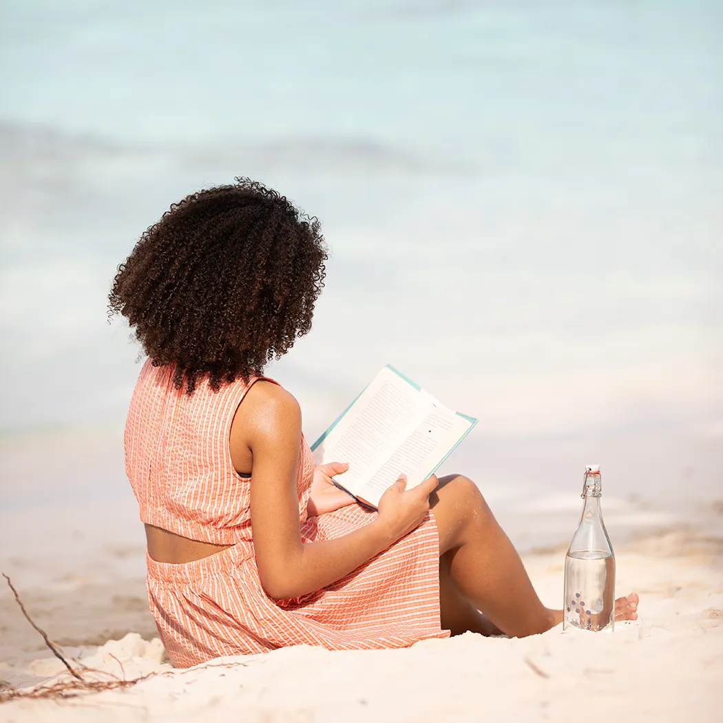 Mädchen sitzt mit Buch am Strand