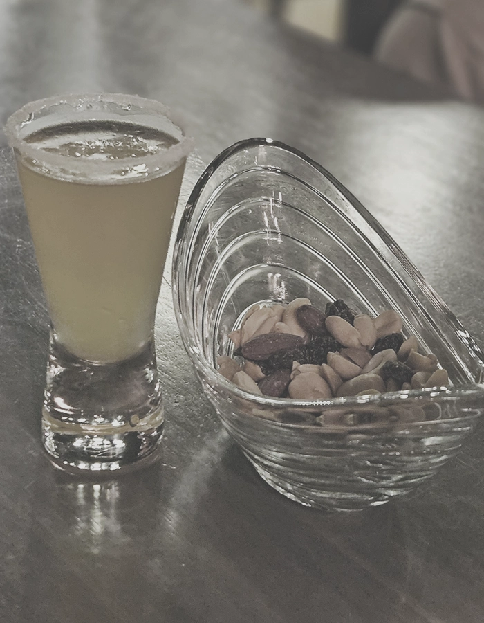 Kleines Schnapsglas mit Getränk und einer Schale Nüssen
