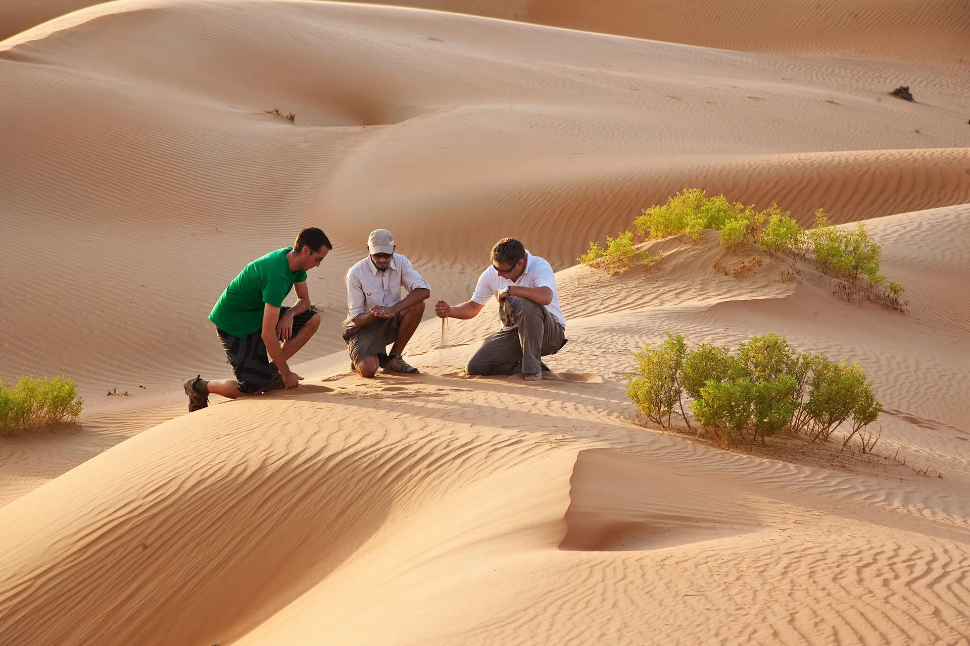 Drei Männer knien im Wüstensand