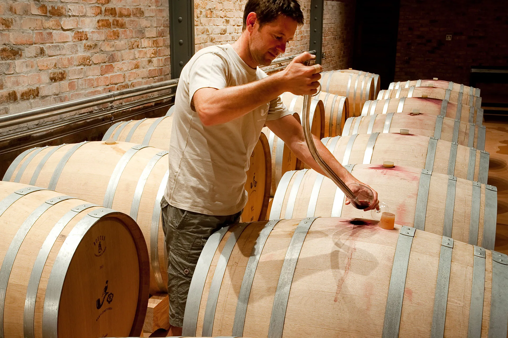Mann schöpft Wein aus Holzfass