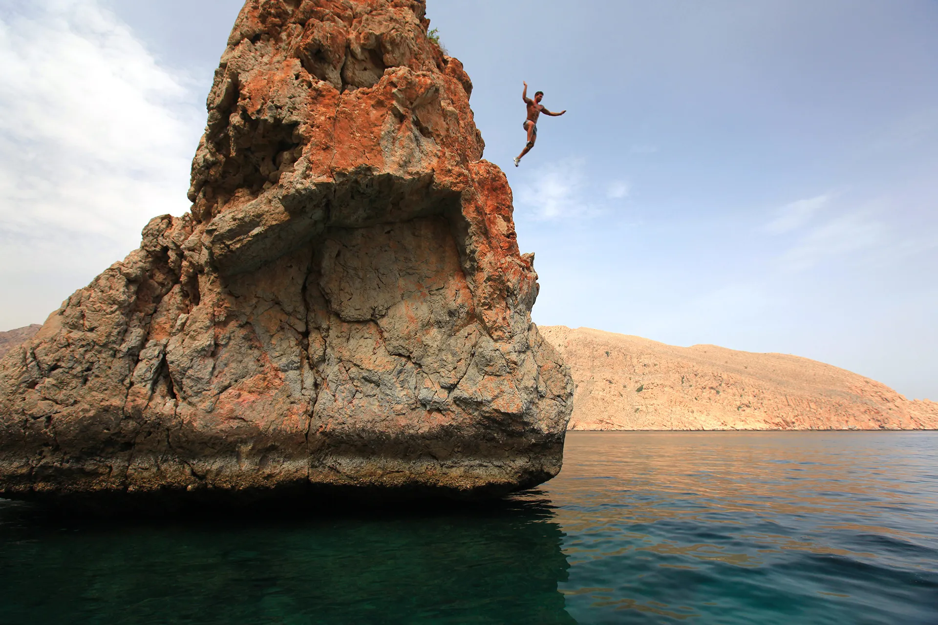 Mann springt von Felsen ins Meer