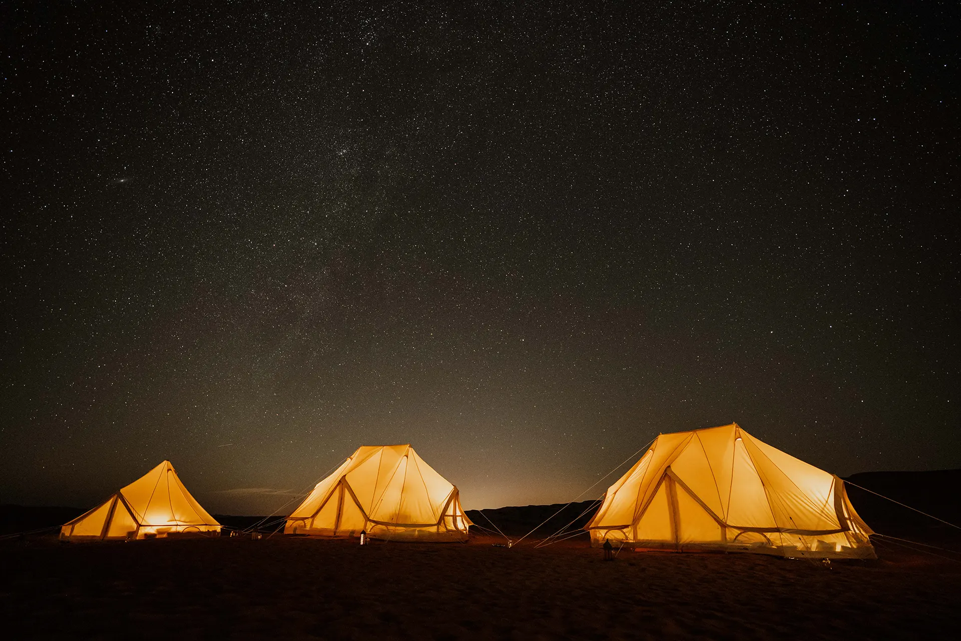 Drei beleuchtete Zelte unter Sternenhimmel