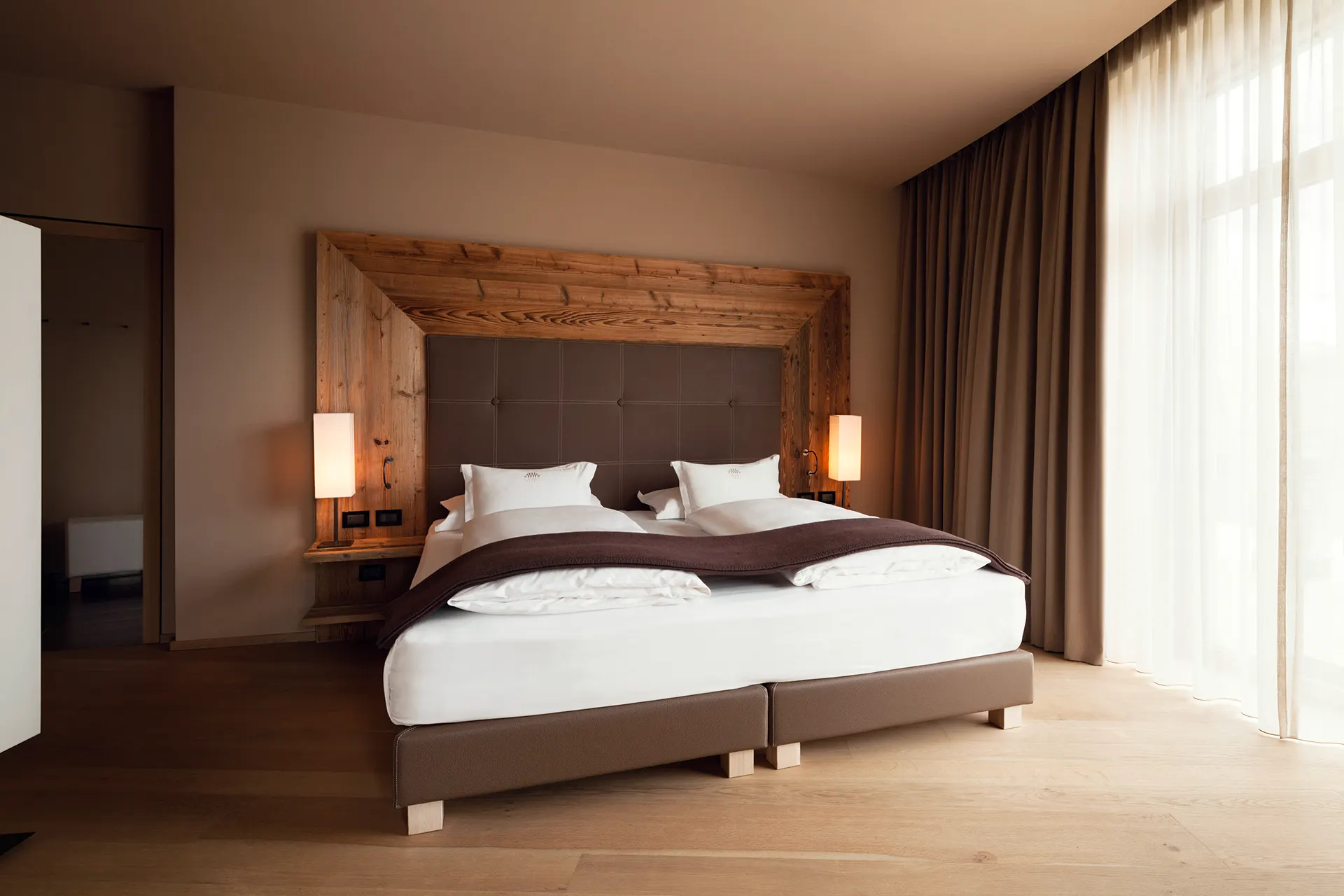Opulentes Doppelbett vor Wand aus Altholz